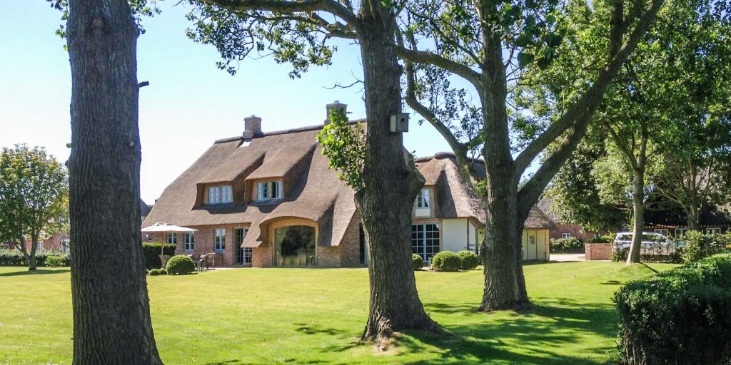 Luxus Ferienhaus auf der Nordseeinsel Föhr: Hausansicht vom Garten mit Blick auf das Reetdachhaus und Bäume